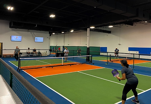 Players on green and orange indoor pickleball courts, from Dill Dinkers’ official franchise website